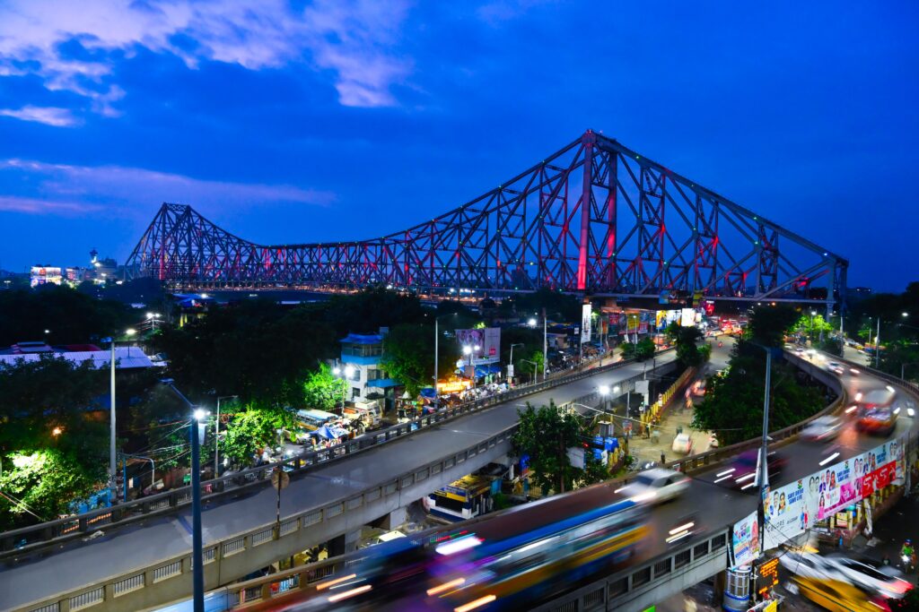Vibrant evening view of Howrah Bridge in Kolkata with dynamic traffic and city lights.