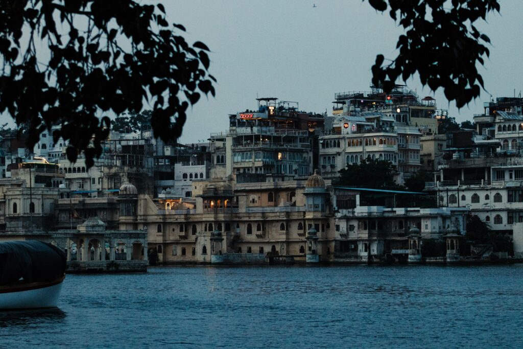 Scenic view of Udaipur's City Palace and surrounding architecture seen from Lake Pichola at dusk.